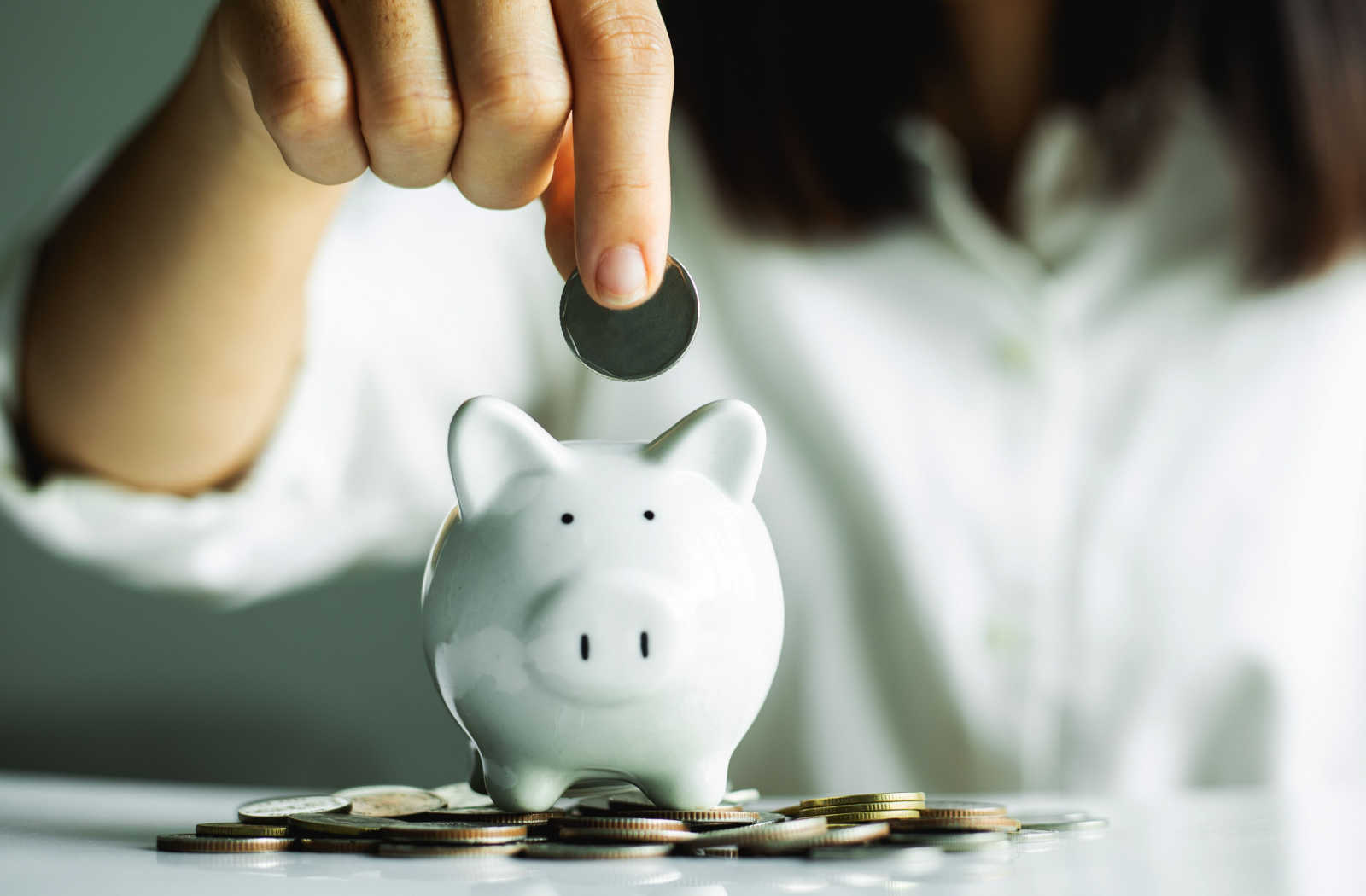 A woman putting a dollar into her white savings piggy bank.