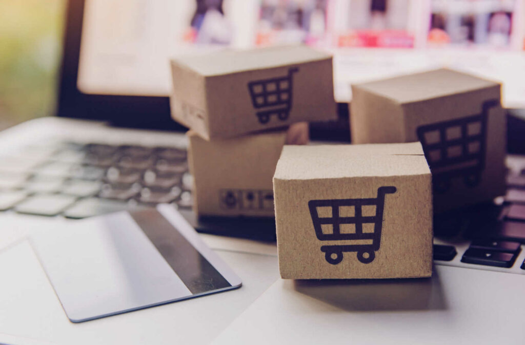 A credit card is placed on a laptop with boxes with a cart drawn on top to show purchases made online.