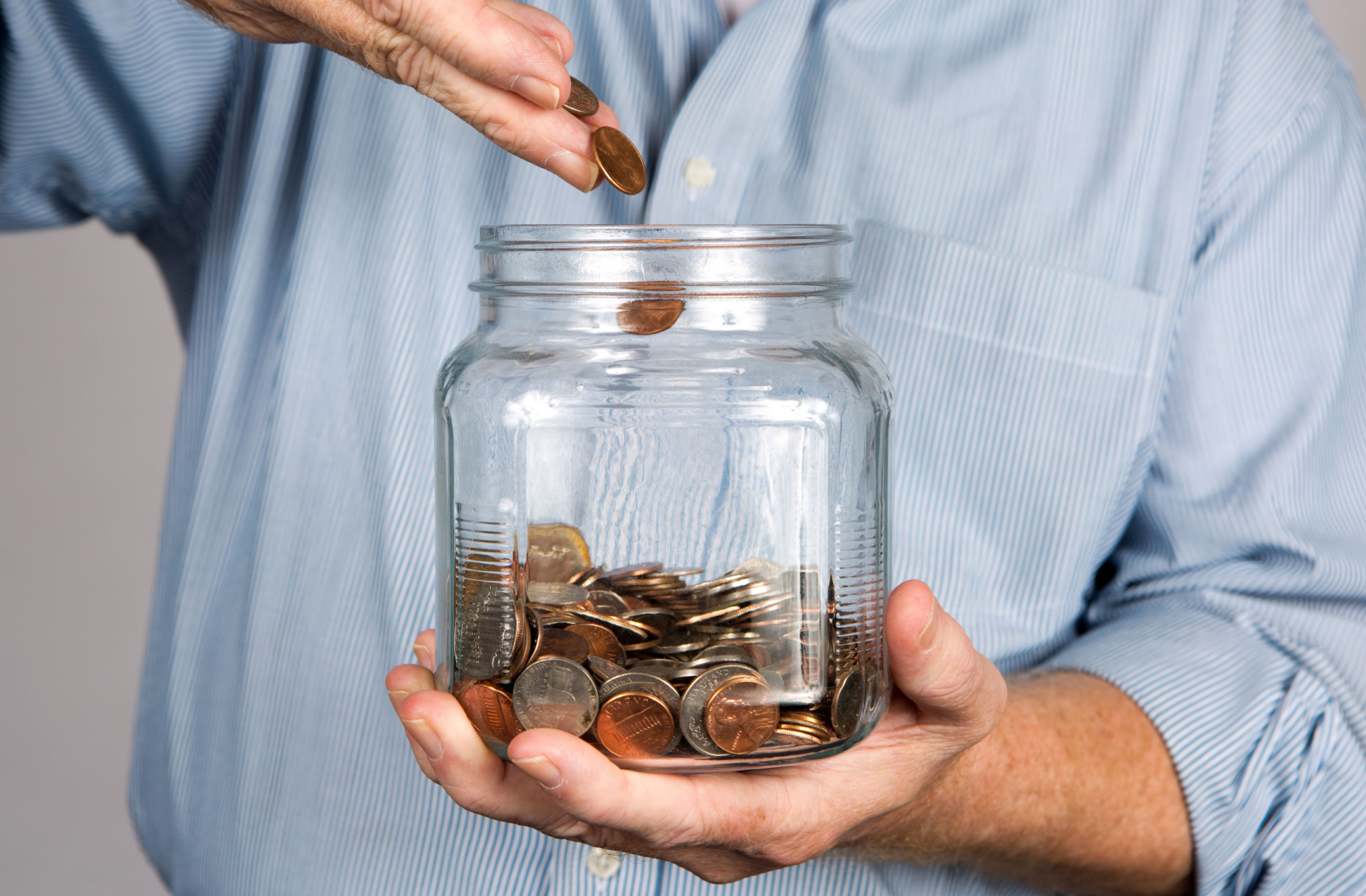 A man drops money into a glass of jar for a savings account.