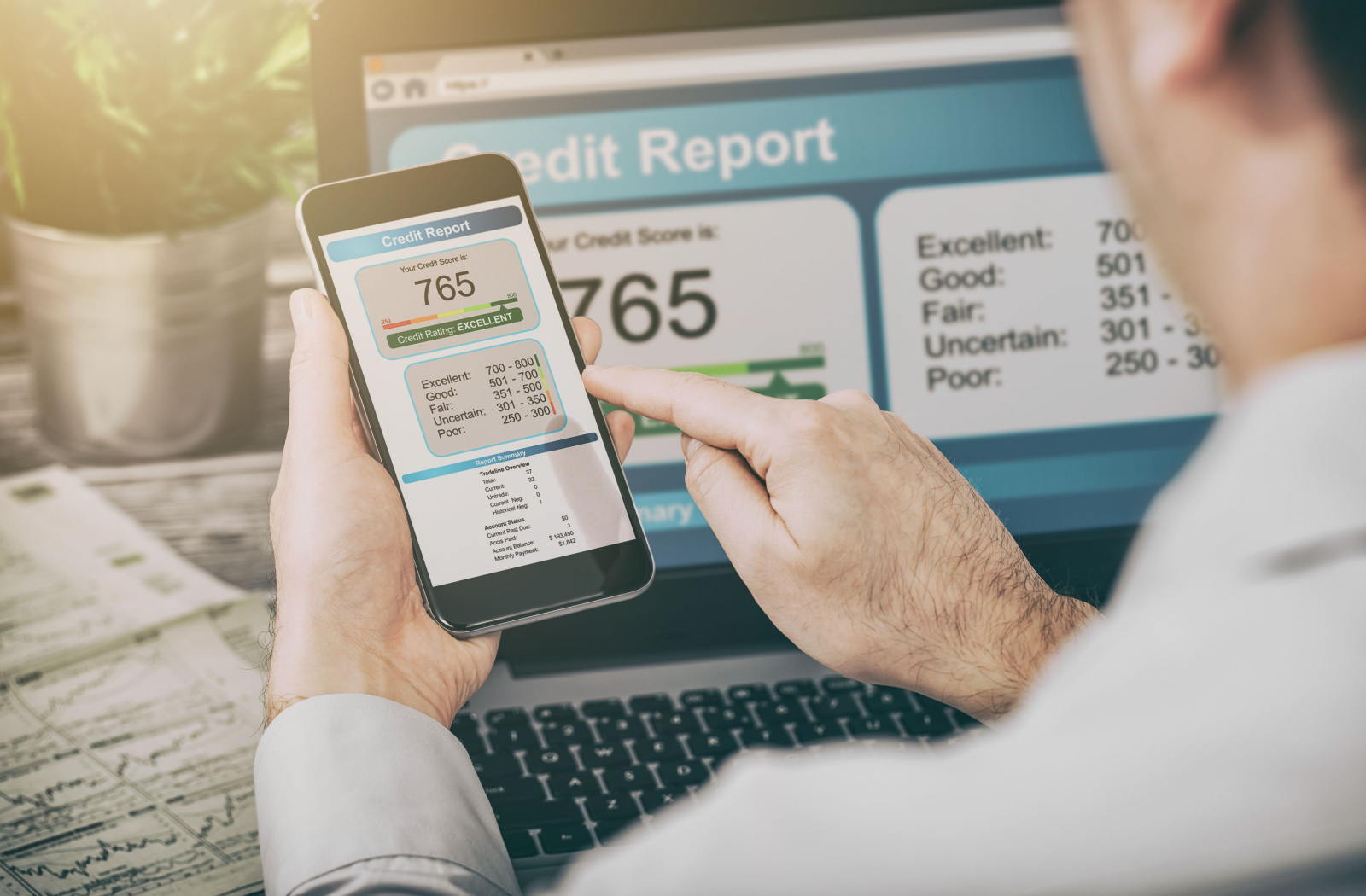 A man checking his credit report using a smartphone and a laptop.