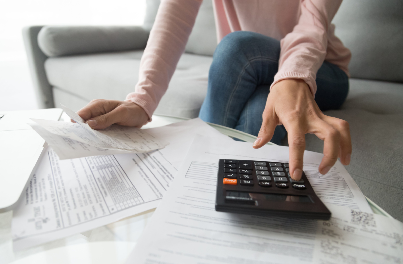 Close-up of a woman's hands typing numbers into a calculator while holding a piece of paper.