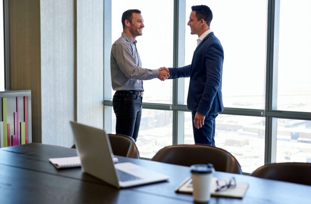 A man smiling and shaking hands with a loan officer, standing by the windows in an office boardroom overlooking the city